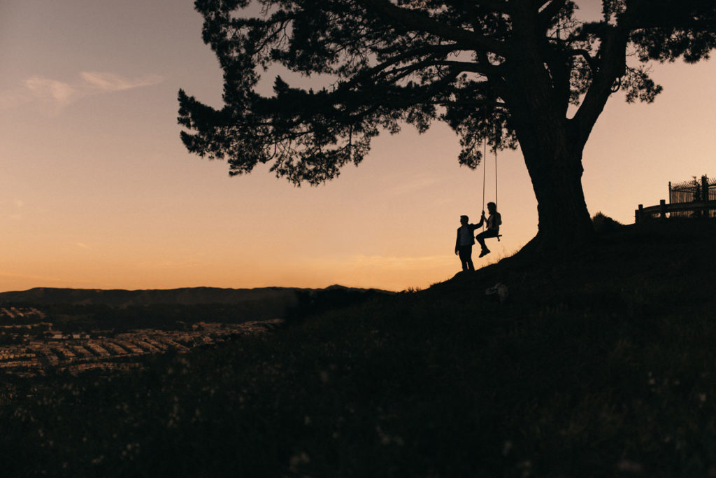 Beautiful sunset photograph at Bernal Heights swing in San Francisco, California, USA. Silhouettes against the golden sundown sky. Engagement couple session in Bay Area. Bernal Heights Park in San Francisco.