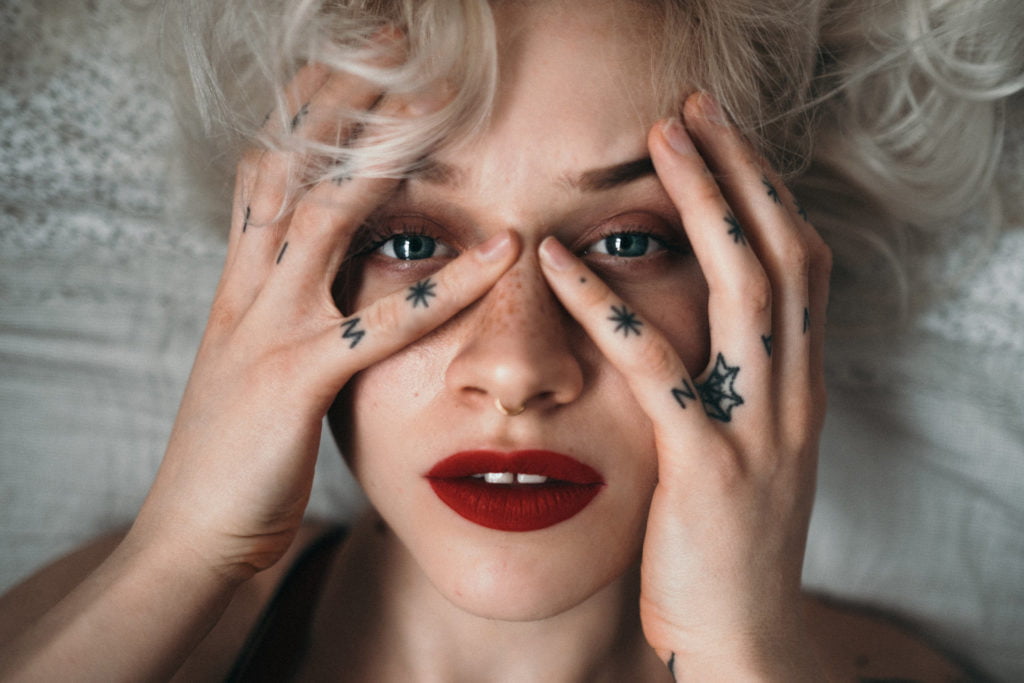 Portrait of a tattooed girl. Emotional portraiture. Finger tatoos, red lips. Freckled blonde girl.
